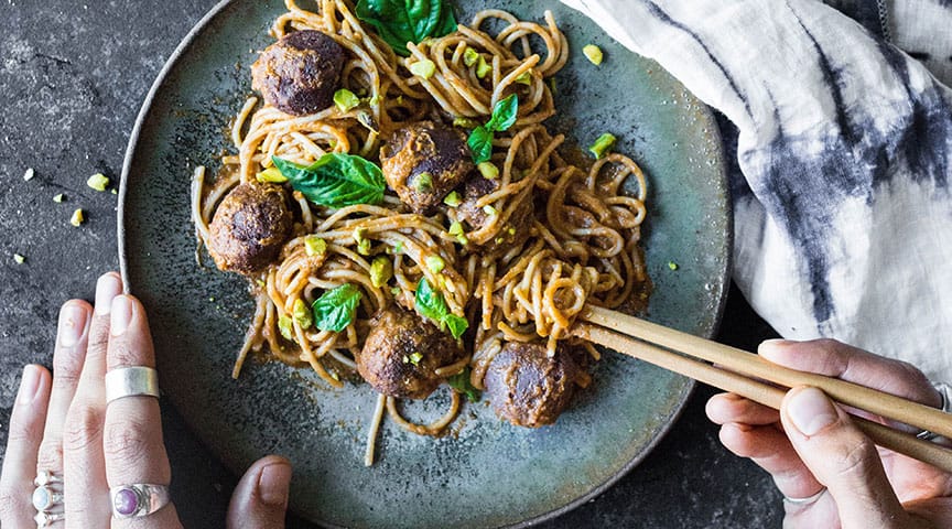 Teff meatballs in a bowl with noodles, hand holding chopsticks